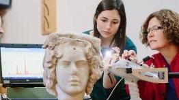 滚球网站的教授和她的学生正在检查一座古代的半身像雕塑.